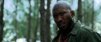 Movie still from “Predators” (2010), directed by Nimród Antal – A man with a beard is standing in the woods; Close Up shot, Low angle