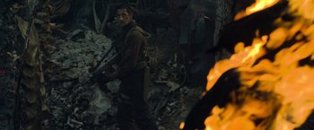 Movie still from “Predators” (2010), directed by Nimród Antal – A man holding a gun while standing next to a fire; Medium shot, Over the shoulder angle