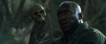 Movie still from “Predators” (2010), directed by Nimród Antal – A man with a skull in the background looking up; Close Up shot, Low angle