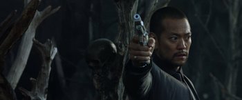 Movie still from “Predators” (2010), directed by Nimród Antal – A man holding a gun in front of a skull; Close Up shot, Low angle