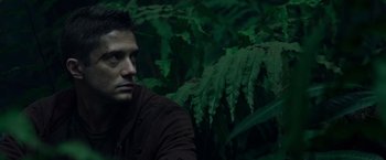 Movie still from “Predators” (2010), directed by Nimród Antal – A person sitting in front of a bush; Close Up shot, Low angle