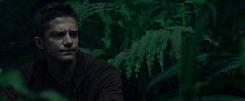 Movie still from “Predators” (2010), directed by Nimród Antal – A man sitting in front of a bush with green leaves; Close Up shot, Over the shoulder angle
