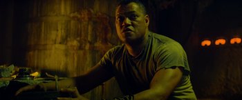 Movie still from “Predators” (2010), directed by Nimród Antal – A person sitting at a table; Close Up shot, Low angle