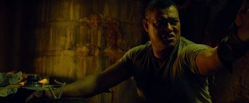 Movie still from “Predators” (2010), directed by Nimród Antal – A man in a green shirt is standing in a room; Close Up shot, Low angle