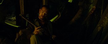 Movie still from “Predators” (2010), directed by Nimród Antal – A man sitting in the dark holding a guitar; Close Up shot, High angle