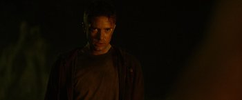 Movie still from “Predators” (2010), directed by Nimród Antal – A man in a brown shirt is standing in the dark; Close Up shot, Low angle