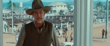 Movie still from “Australia” (2008), directed by Baz Luhrmann – A man in a hat and vest standing in front of a window; Medium shot, Over the shoulder angle