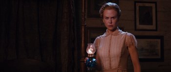 Movie still from “Australia” (2008), directed by Baz Luhrmann – A woman standing next to an oil lamp in a dark room; Medium shot, Over the shoulder angle