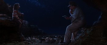 Movie still from “Australia” (2008), directed by Baz Luhrmann – A man sitting on the ground while using a cell phone in front of a herd of sheep; Wide shot, Low angle
