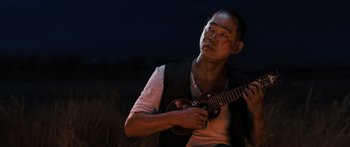 Movie still from “Australia” (2008), directed by Baz Luhrmann – A man holding a guitar while standing in a field at night; Close Up shot, Over the shoulder angle