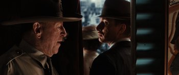 Movie still from “Australia” (2008), directed by Baz Luhrmann – A man in a suit and a man in a hat talking to each other in front of a curtain; Close Up shot, Over the shoulder angle