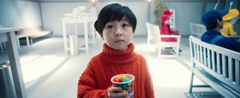 Movie still from “Prisoners of the Ghostland” (2021), directed by Sion Sono – A young boy holding a cup of candy; Close Up shot, Over the shoulder angle