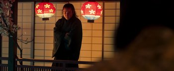 Movie still from “Prisoners of the Ghostland” (2021), directed by Sion Sono – A person standing in front of a wall with a lamp in front of them; Medium shot, Low angle