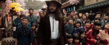 Movie still from “Prisoners of the Ghostland” (2021), directed by Sion Sono – A group of people gathered around a man wearing a hat; Medium shot, Over the shoulder angle