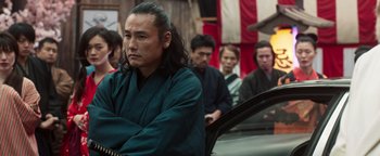 Movie still from “Prisoners of the Ghostland” (2021), directed by Sion Sono – A group of people sitting in a room; Medium shot, Low angle
