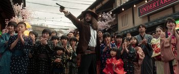 Movie still from “Prisoners of the Ghostland” (2021), directed by Sion Sono – A group of people in costumes with a man holding a gun in his hand; Medium shot, Low angle