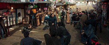 Movie still from “Prisoners of the Ghostland” (2021), directed by Sion Sono – A group of people in a courtyard with swords in their hands; Wide shot, High angle