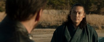 Movie still from “Prisoners of the Ghostland” (2021), directed by Sion Sono – A woman in a black robe talking to a man in a green robe; Close Up shot, Over the shoulder angle