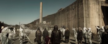 Movie still from “Prisoners of the Ghostland” (2021), directed by Sion Sono – A group of people standing next to an abandoned factory; Extreme Wide shot, High angle