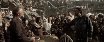 Movie still from “Prisoners of the Ghostland” (2021), directed by Sion Sono – A group of people standing around a table; Wide shot, Over the shoulder angle
