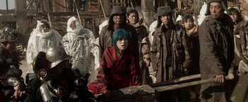 Movie still from “Prisoners of the Ghostland” (2021), directed by Sion Sono – A group of people standing around a wooden structure; Medium shot, High angle