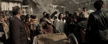 Movie still from “Prisoners of the Ghostland” (2021), directed by Sion Sono – A group of people standing around a cart; Medium shot, Over the shoulder angle