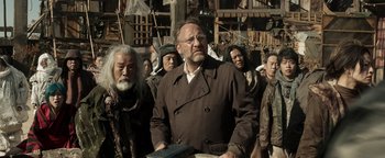 Movie still from “Prisoners of the Ghostland” (2021), directed by Sion Sono – A group of people standing around a building; Medium shot, Low angle