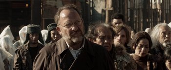 Movie still from “Prisoners of the Ghostland” (2021), directed by Sion Sono – A man with a beard and glasses in front of a group of people; Close Up shot, Over the shoulder angle