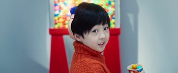 Movie still from “Prisoners of the Ghostland” (2021), directed by Sion Sono – A little girl wearing an orange sweater and a blue hairbrush in her hair; Close Up shot, Overhead angle