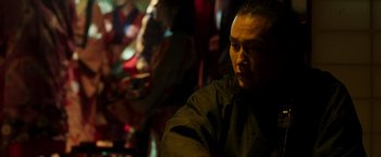 Movie still from “Prisoners of the Ghostland” (2021), directed by Sion Sono – A man sitting in front of a group of people; Close Up shot, Over the shoulder angle
