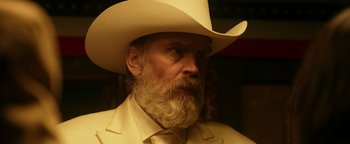 Movie still from “Prisoners of the Ghostland” (2021), directed by Sion Sono – A man with a beard wearing a white cowboy hat; Close Up shot, Over the shoulder angle