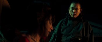 Movie still from “Prisoners of the Ghostland” (2021), directed by Sion Sono – Two people sitting in a dark room , one of whom is wearing a black jacket; Close Up shot, Over the shoulder angle