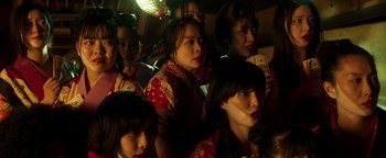 Movie still from “Prisoners of the Ghostland” (2021), directed by Sion Sono – A group of women sitting next to each other in a room; Close Up shot, High angle