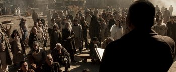 Movie still from “Prisoners of the Ghostland” (2021), directed by Sion Sono – A group of people standing around a bench; Wide shot, High angle