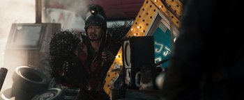 Movie still from “Prisoners of the Ghostland” (2021), directed by Sion Sono – A man wearing a helmet is standing in front of a carnival ride; Medium shot, Low angle