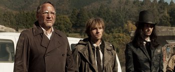 Movie still from “Prisoners of the Ghostland” (2021), directed by Sion Sono – A man standing next to another man near a forest; Medium shot, Low angle