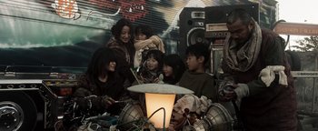 Movie still from “Prisoners of the Ghostland” (2021), directed by Sion Sono – A group of children sitting around a table; Medium shot, Low angle