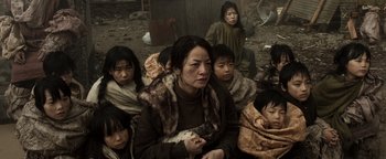Movie still from “Prisoners of the Ghostland” (2021), directed by Sion Sono – A group of people sitting in a pile of dirt; Medium shot, High angle