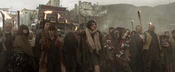 Movie still from “Prisoners of the Ghostland” (2021), directed by Sion Sono – A group of people standing in a crowd near a clock tower; Wide shot, Low angle