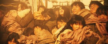Movie still from “Prisoners of the Ghostland” (2021), directed by Sion Sono – A group of people that are sitting together; Medium shot, High angle
