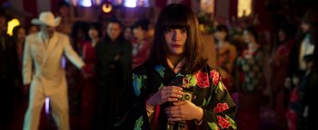 Movie still from “Prisoners of the Ghostland” (2021), directed by Sion Sono – A woman in a kimono holding a camera in front of a group of onlookers; Medium shot, Low angle