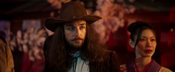 Movie still from “Prisoners of the Ghostland” (2021), directed by Sion Sono – A man with long hair wearing a cowboy hat; Close Up shot, Low angle