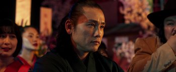 Movie still from “Prisoners of the Ghostland” (2021), directed by Sion Sono – A man with long black hair wearing a black robe; Close Up shot, Low angle