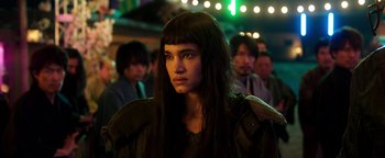 Movie still from “Prisoners of the Ghostland” (2021), directed by Sion Sono – A woman with long black hair wearing a green jacket; Close Up shot, Low angle