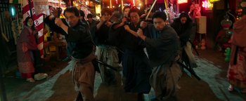 Movie still from “Prisoners of the Ghostland” (2021), directed by Sion Sono – A group of men in traditional garb holding swords; Wide shot, Low angle