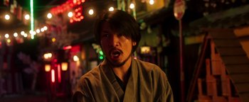Movie still from “Prisoners of the Ghostland” (2021), directed by Sion Sono – A man in a robe is making a funny face; Close Up shot, Low angle