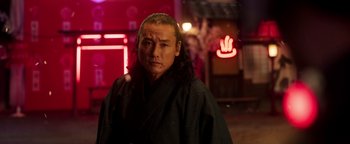 Movie still from “Prisoners of the Ghostland” (2021), directed by Sion Sono – A man with long hair wearing a black robe; Close Up shot, Low angle