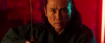 Movie still from “Prisoners of the Ghostland” (2021), directed by Sion Sono – A person holding a sword; Close Up shot, Low angle