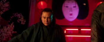 Movie still from “Prisoners of the Ghostland” (2021), directed by Sion Sono – A man in a black robe standing in front of a red wall; Close Up shot, Low angle