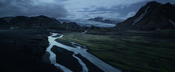A view of a valley with a river running through it and a mountain in the background